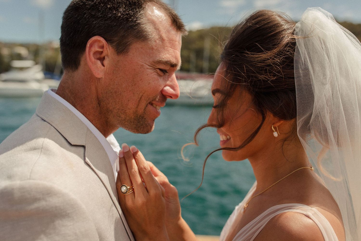 A tender moment between newlyweds against a backdrop of sparkling water and boats.