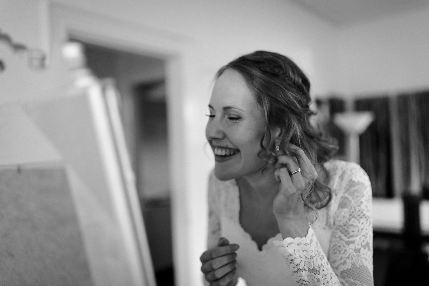 Black and white photo showing someone laughing and getting ready in a bright room with lace details visible.