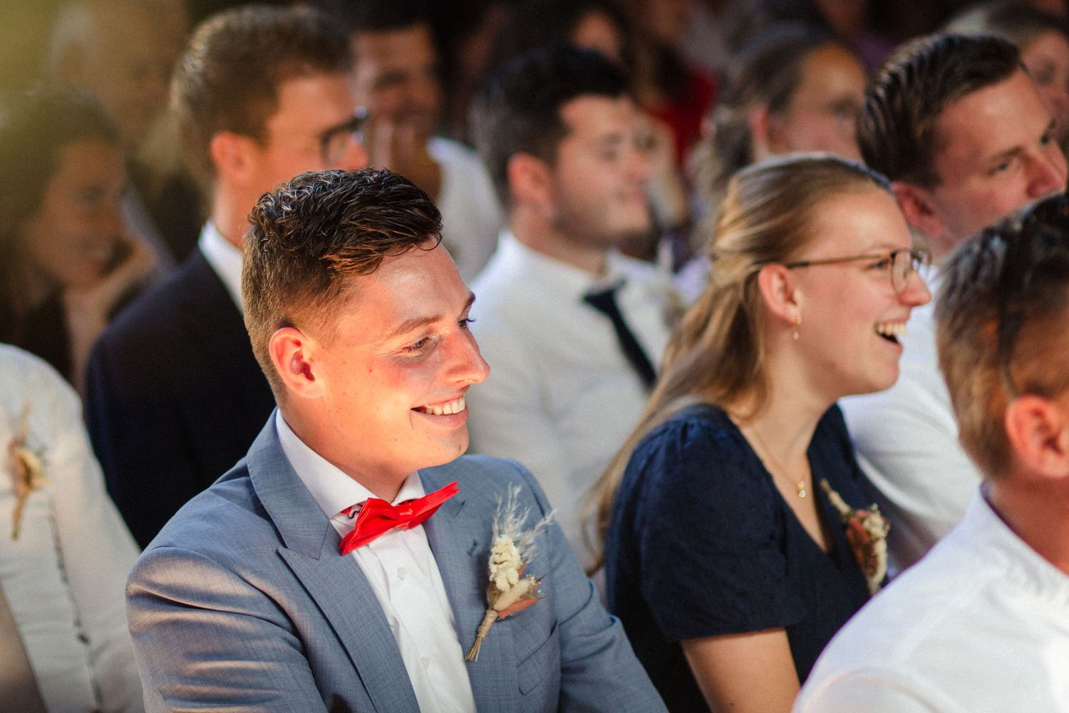 Wedding guests share a joyful moment during the ceremony as they sit together wearing formal attire.