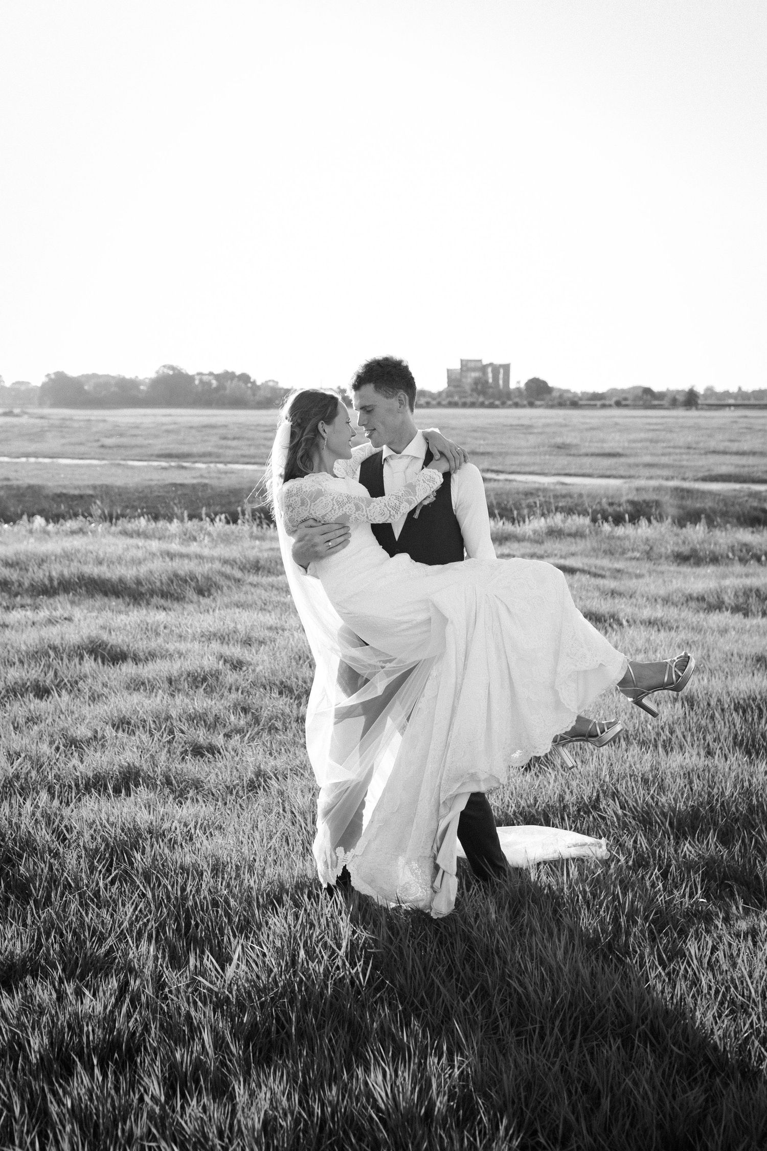 A romantic black and white wedding photo of a couple dancing in a grassy field at sunset.