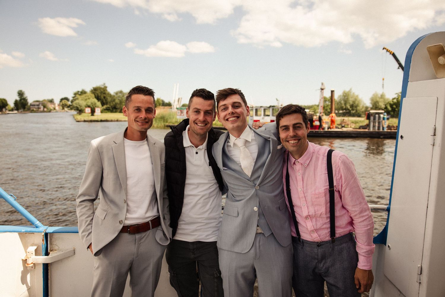 Group of friends in formal attire posing together on boat dock during sunset.