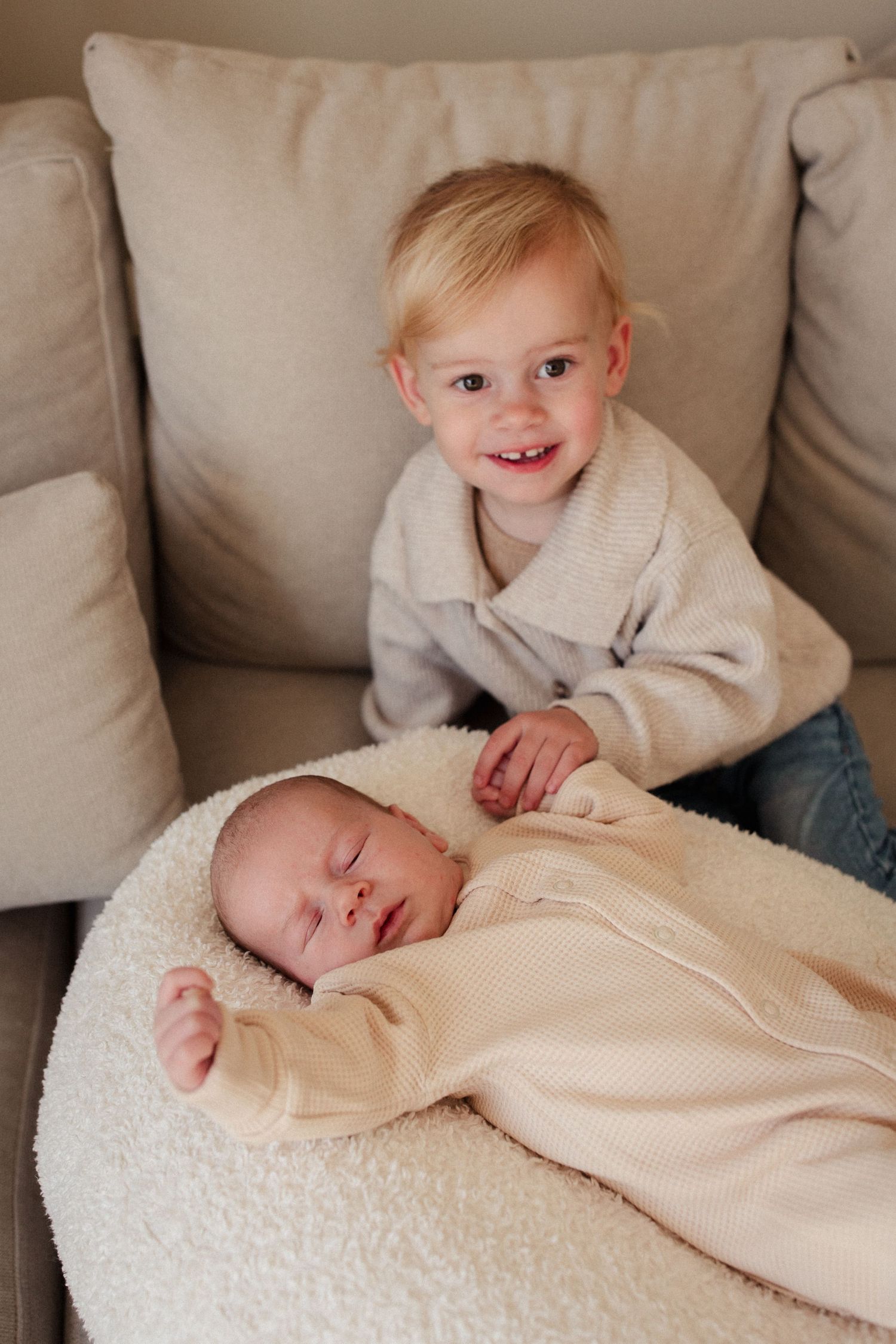 Sweet sibling moment on a gray couch with cushions.