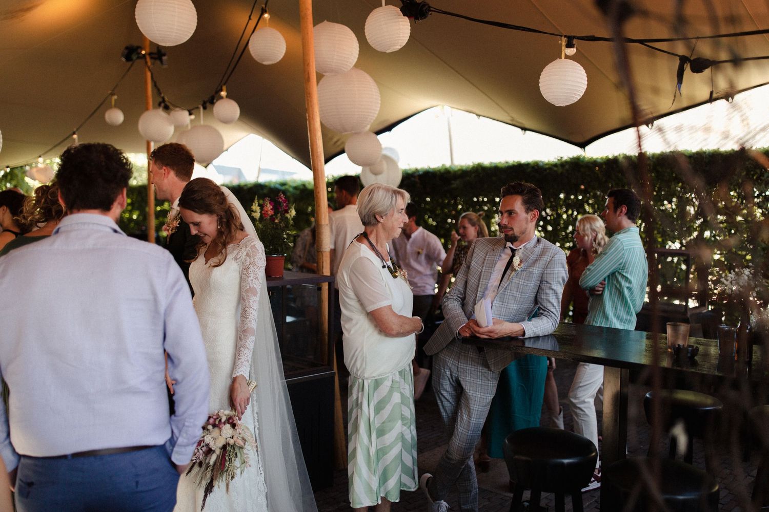 Wedding guests mingle at an outdoor reception with white paper lanterns and umbrellas decorating the space.