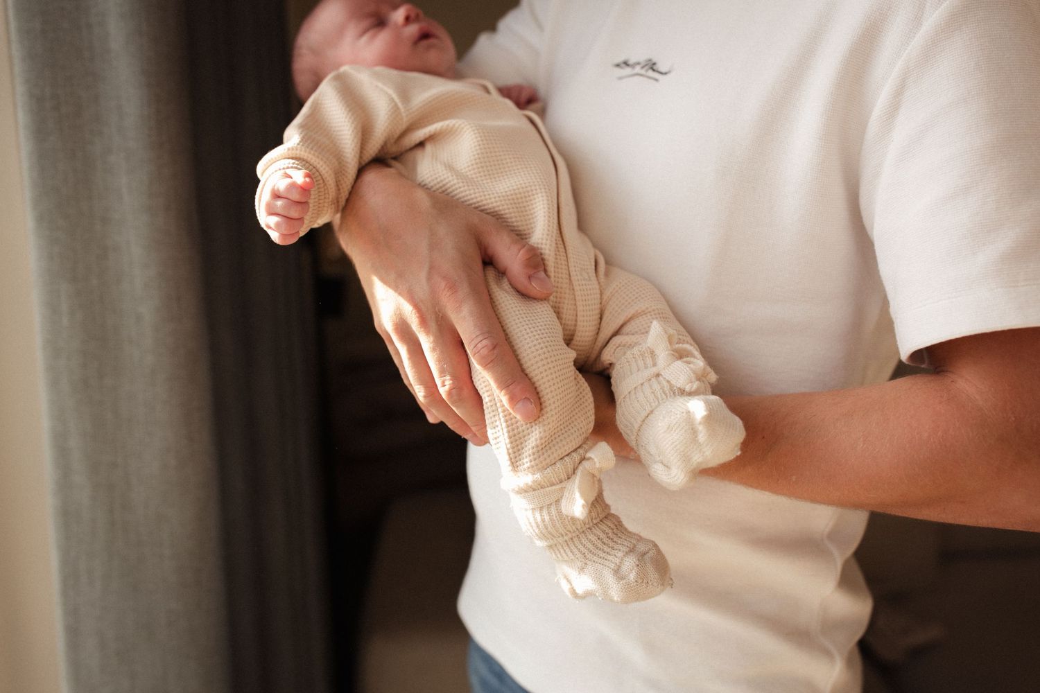 Parent holding sleeping newborn baby wearing cream colored onesie.