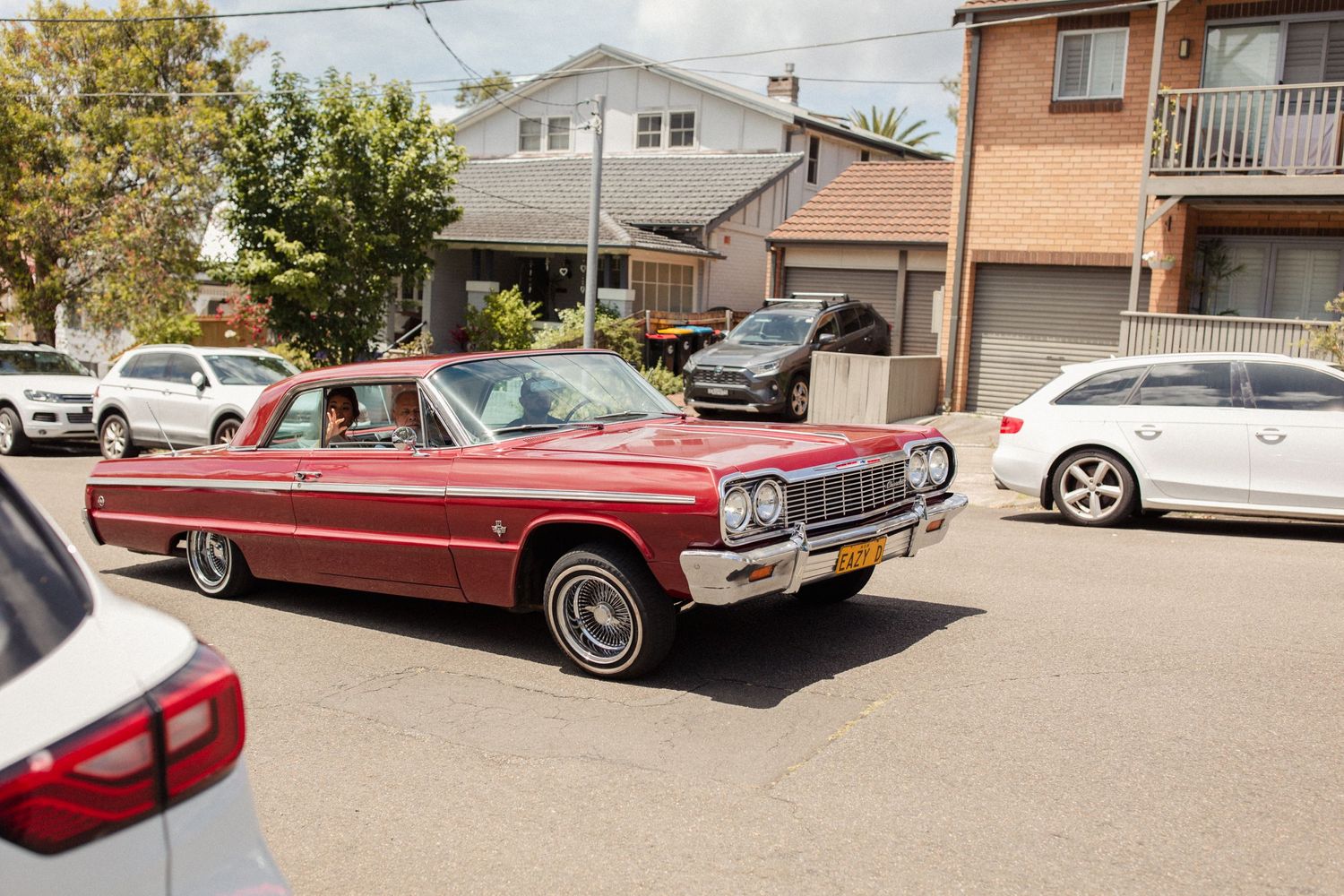 Classic red Chevrolet Impala parked on a suburban street among modern cars.