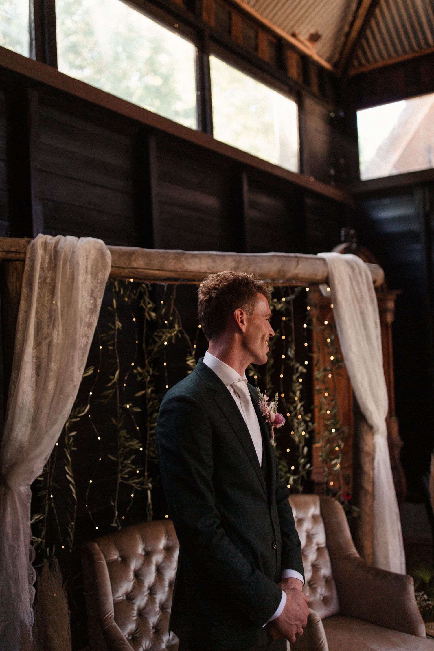 A rustic wooden venue interior decorated with white drapes and string lights creates an elegant wedding atmosphere.