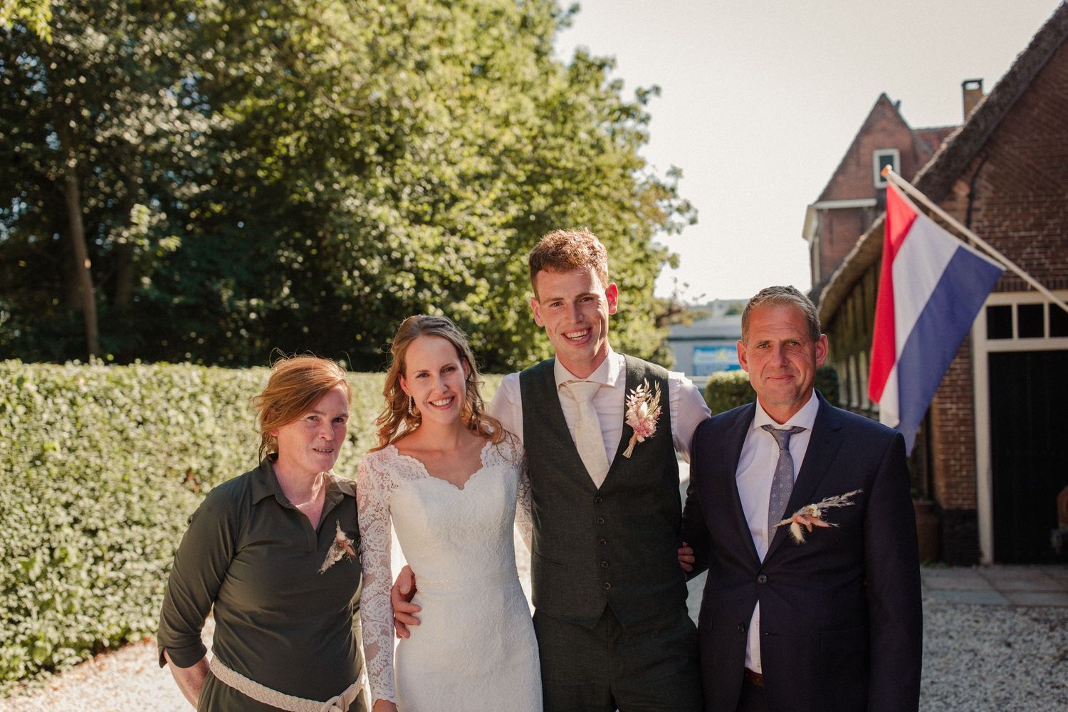 Wedding celebration group poses together outdoors on a sunny day with Dutch flag in background.