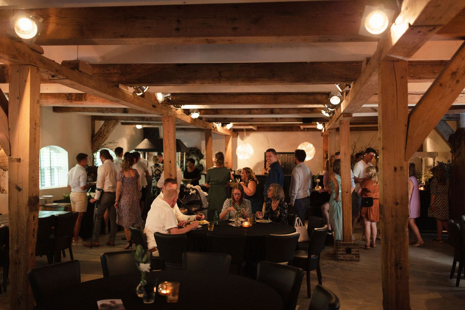A rustic basement venue with wooden beams and soft lighting where people gather around a piano player performing music.