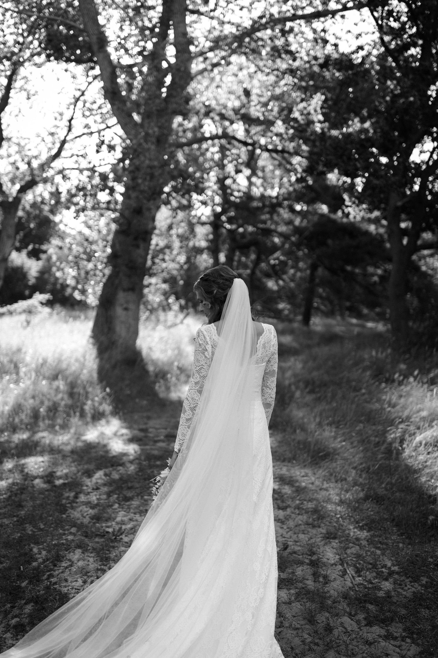 A flowing white wedding veil and gown trail behind in a dreamy black and white forest scene.