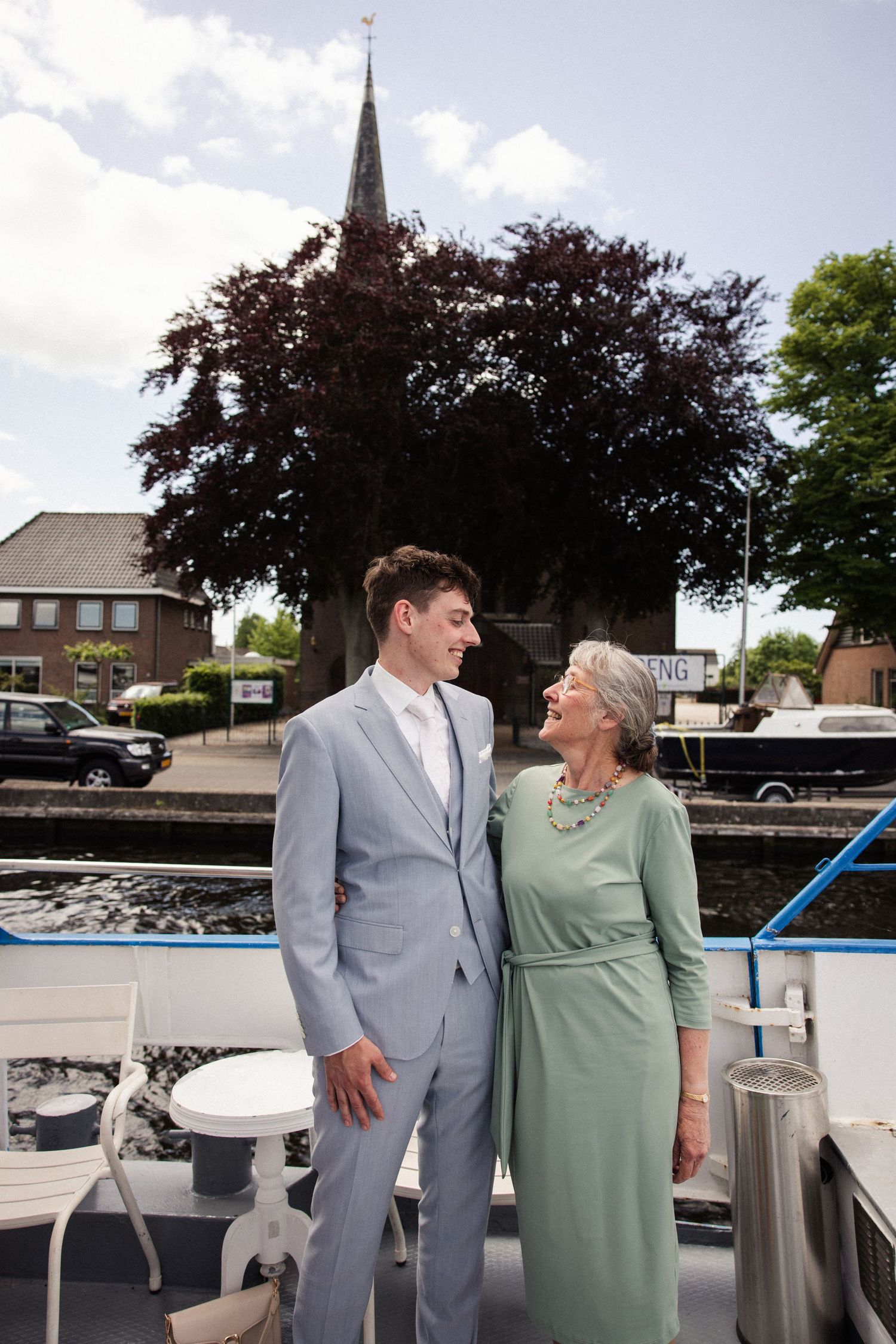 Wedding party members enjoying a moment together on a boat with church spire in background.