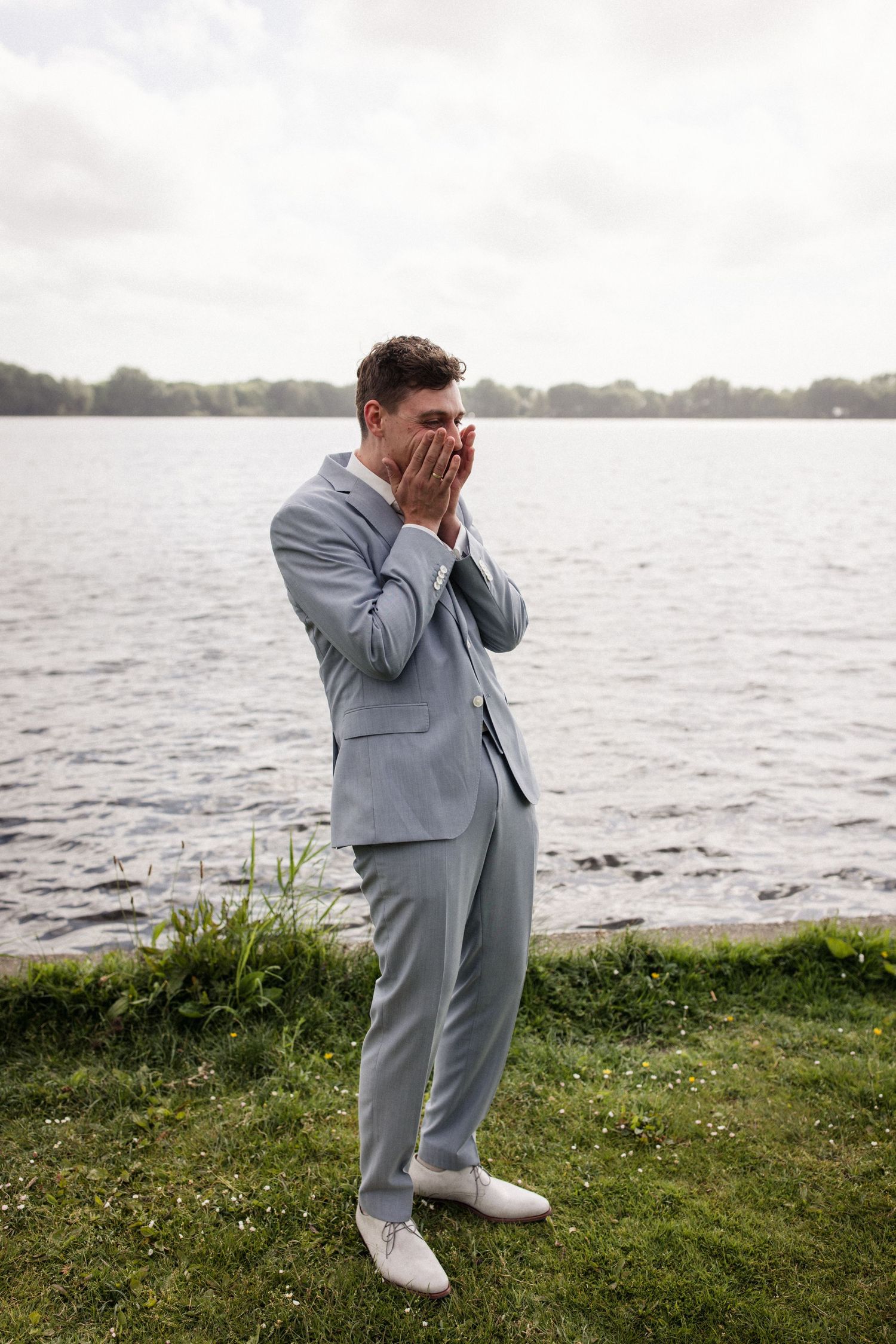 Person in light gray suit shows emotional reaction by waterfront.