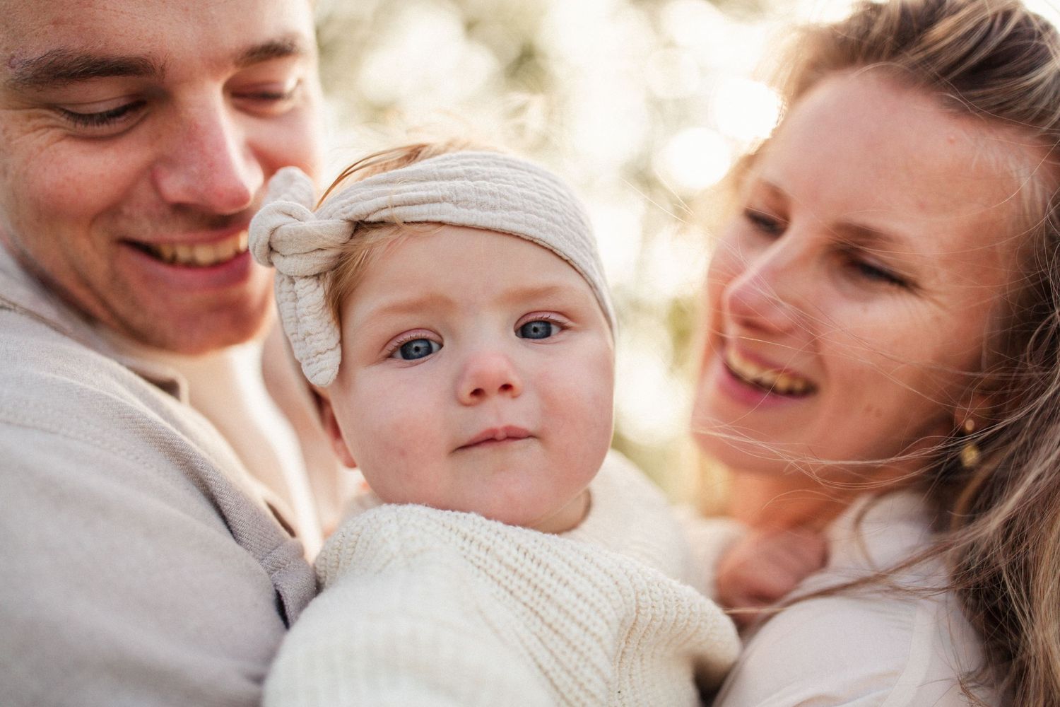 Family portrait in soft natural light with baby wearing a light colored cap.
