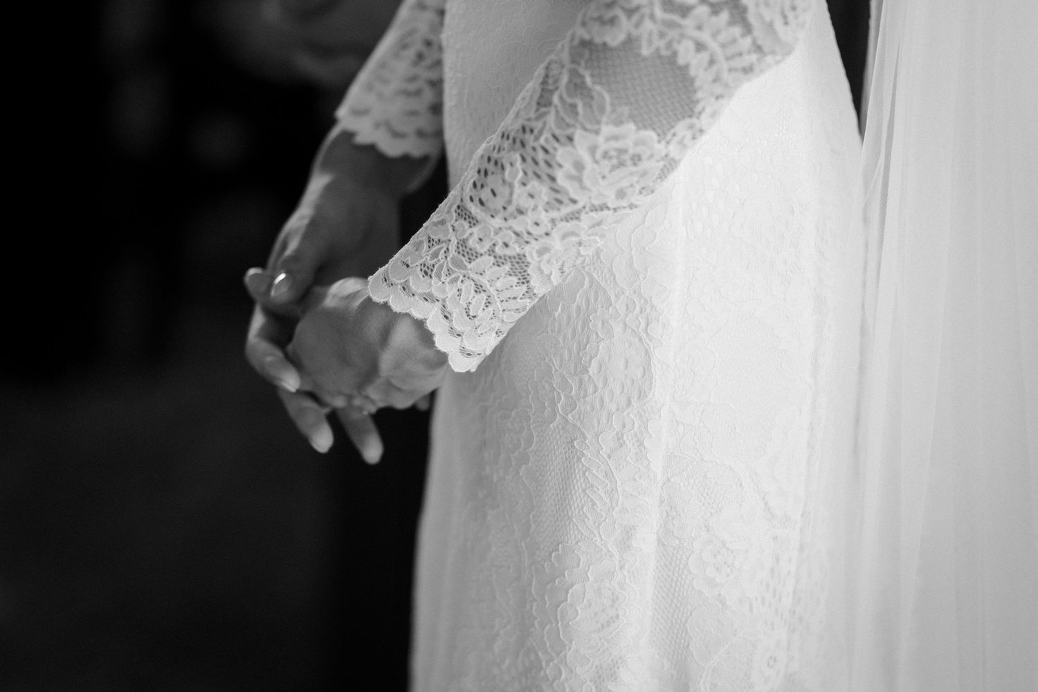 Black and white close-up detail of delicate lace sleeve and fabric from a wedding dress.