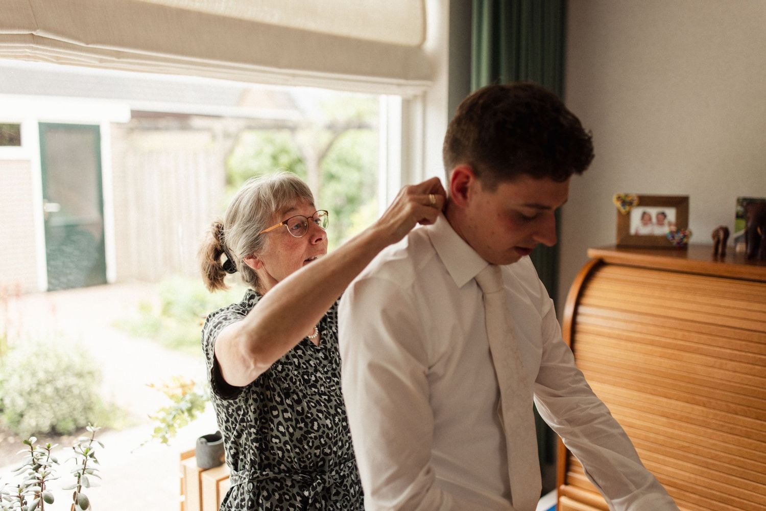 A person helps adjust formal attire in preparation for a special event indoors.