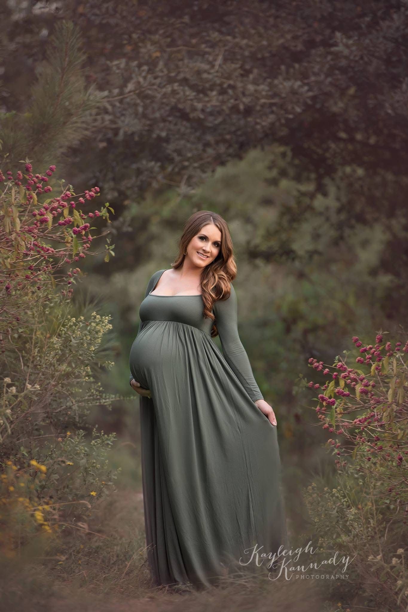 Maternity portrait of expecting mom in sage green dress smiling in wildflowers – timeless outdoor maternity photography by Kayleigh Kannady.