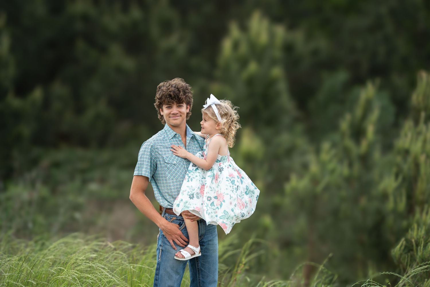 Big brother holding baby sister with a big smile in a green field in tomball texas