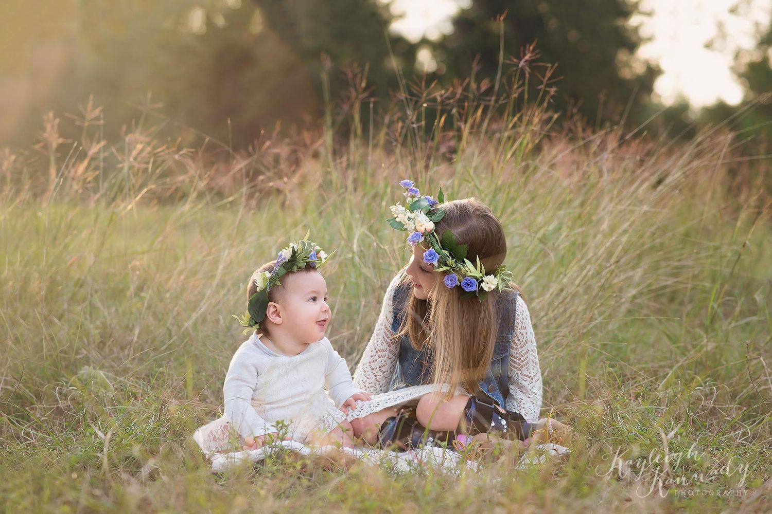 Two sisters wearing flower crowns sitting in field at golden hour – whimsical child photography outdoors by Kayleigh Kannady photography
