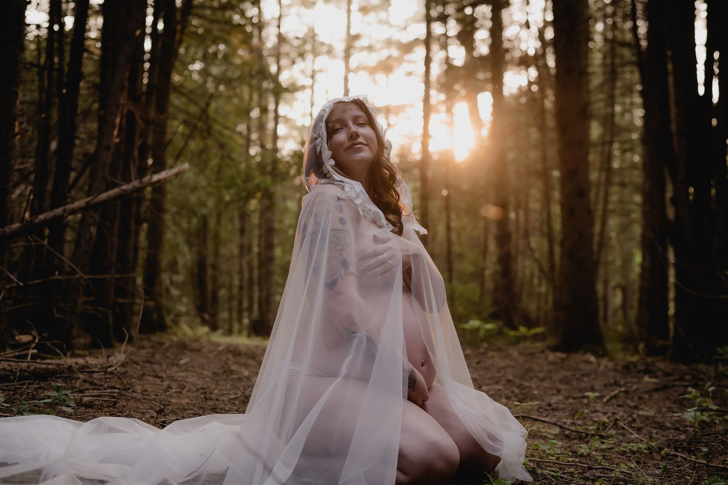 Maternity photography session in a sunlit forest with golden hour lighting filtering through trees. Maternity photographer Ontario