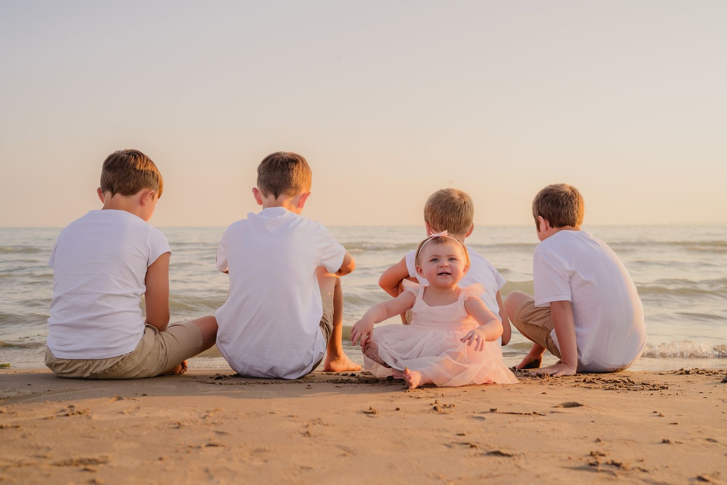A family sits together on the beach at sunset wearing coordinated white outfits.