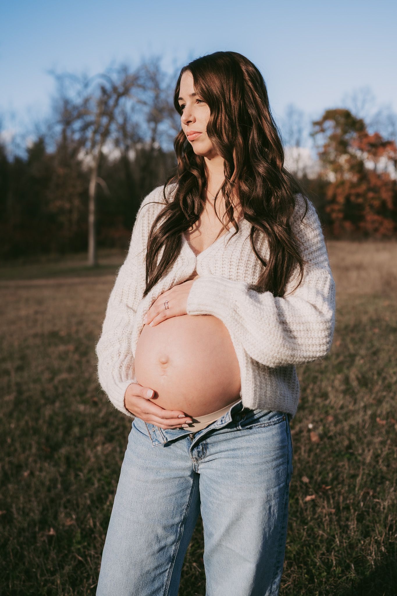 A series of maternity photos showing a pregnant woman in a white sweater and jeans standing in an autumn field. Maternity photographer Ontar