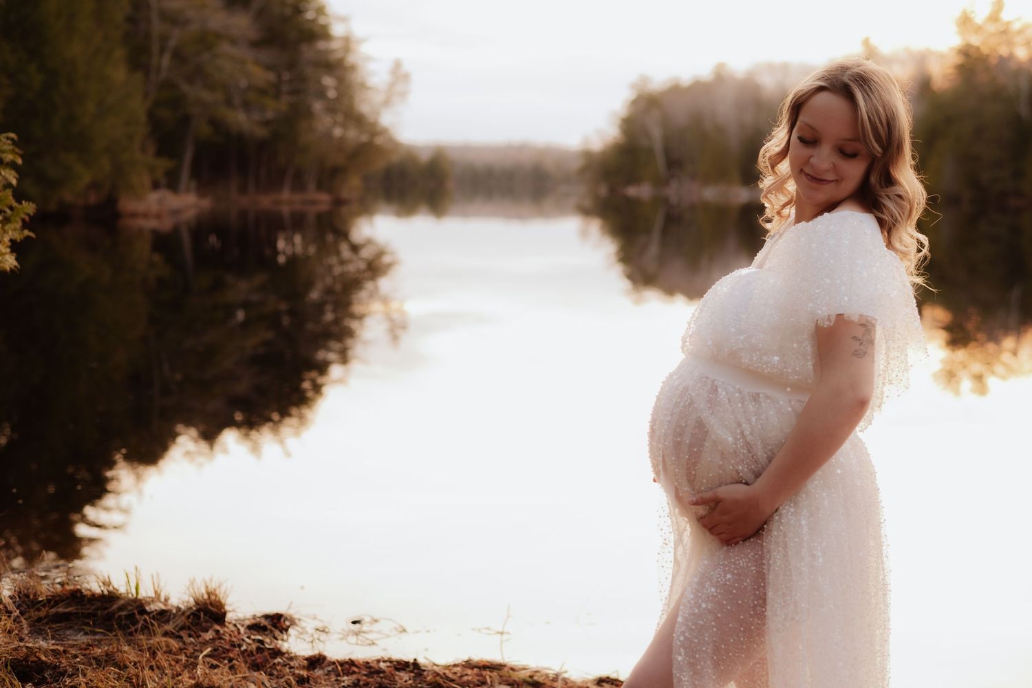 Maternity photos by a serene lake during golden hour with flowing white dress. Maternity photographer Ontario