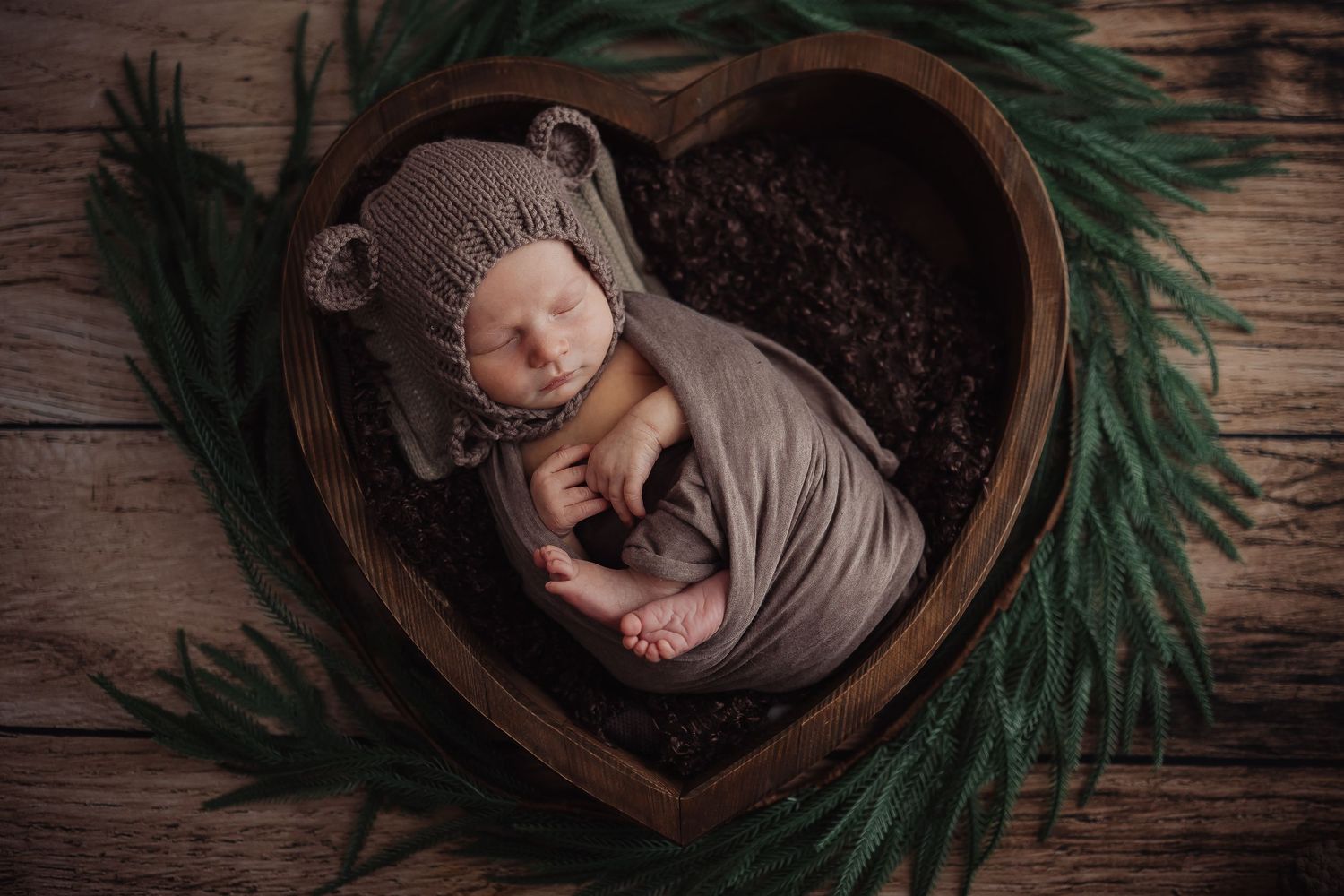 Overhead view of sleeping newborn in wooden bowl with evergreen branch decoration.