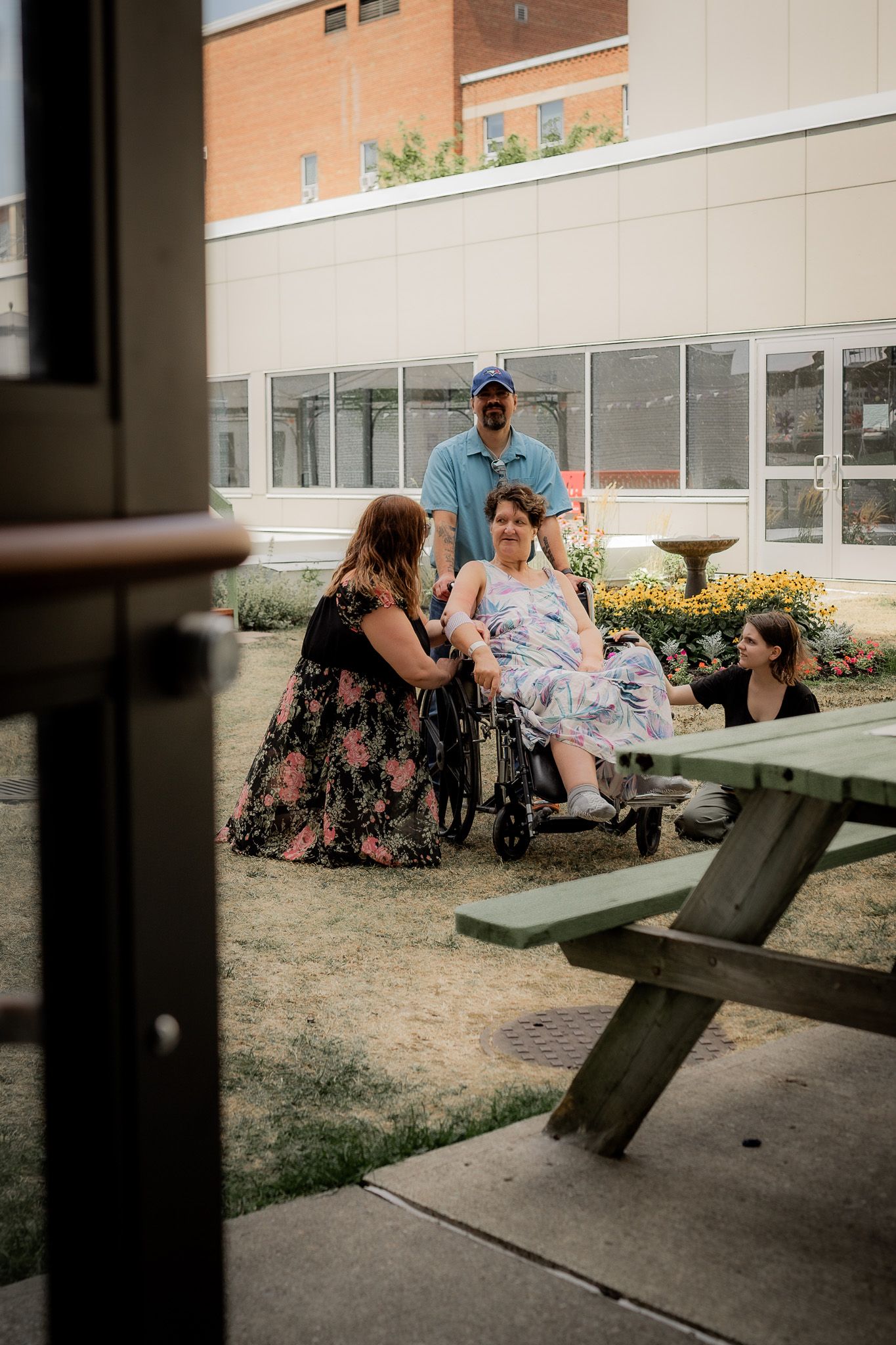 People gathered together on outdoor picnic benches near a brick building on a sunny day.