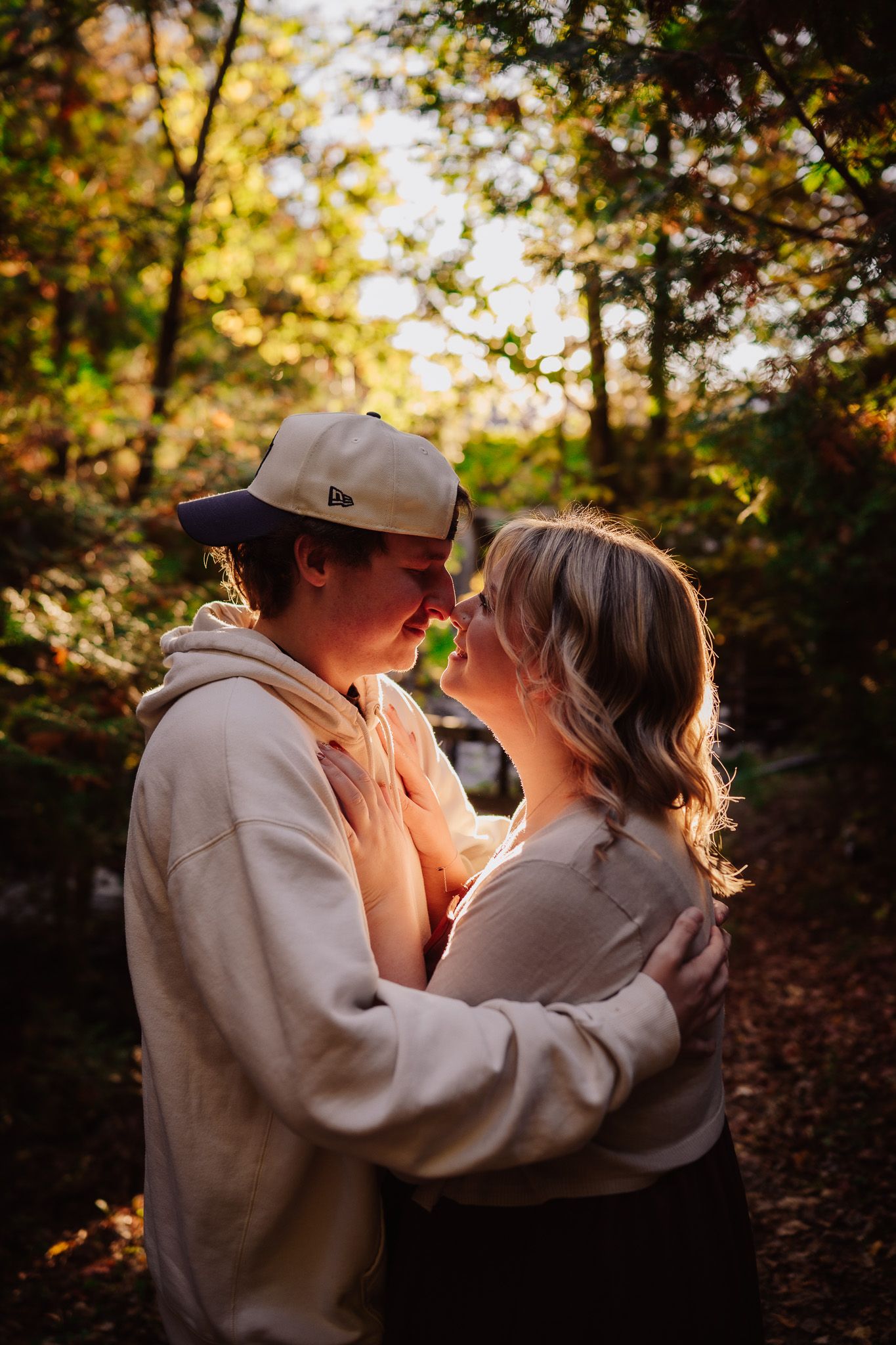 A romantic autumn scene in the woods with golden sunlight filtering through the trees during a tender embrace.