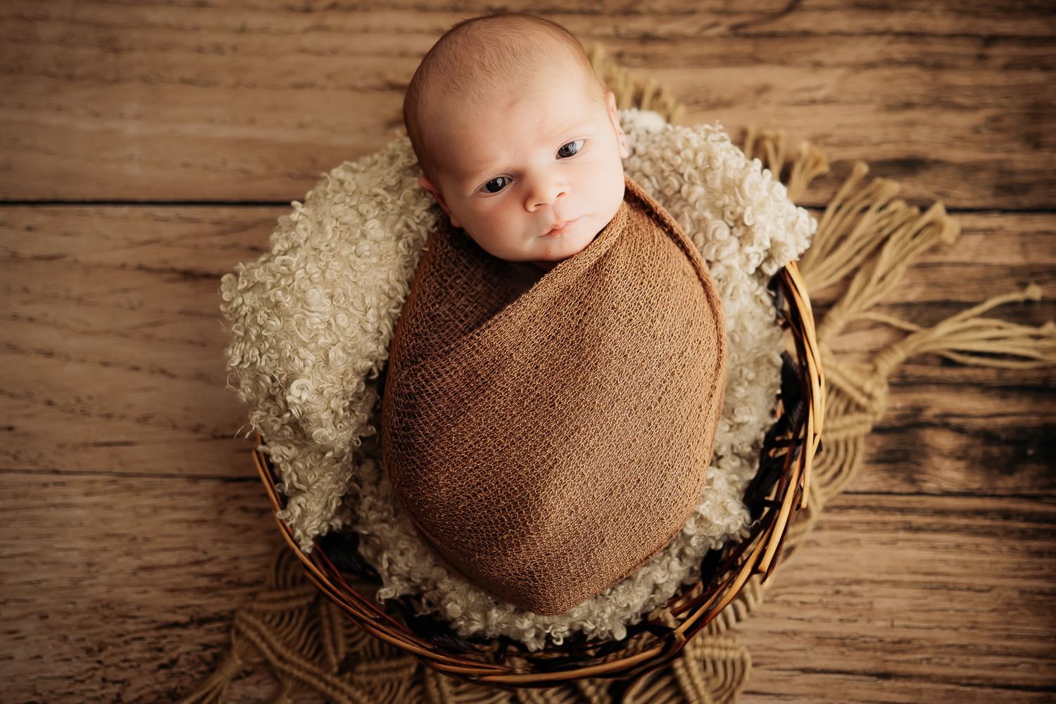 A series of newborn baby photos in brown tones showing an infant wrapped in soft fabric on rustic wooden backgrounds.
