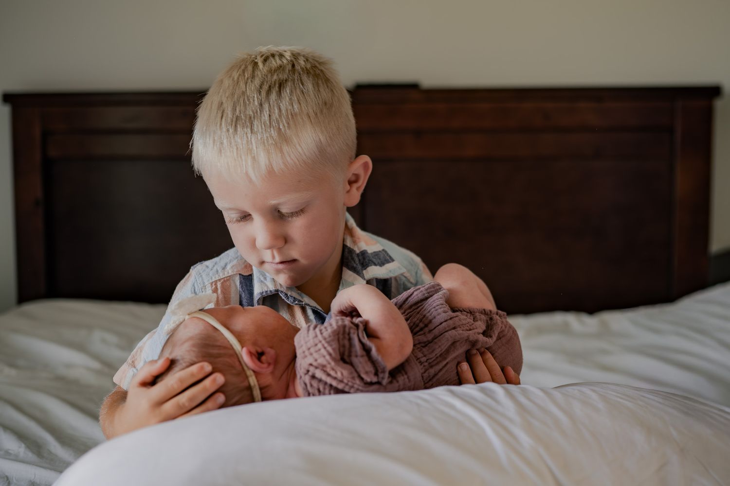 Child lying on white bedding while reading a book with soft natural lighting from the side.