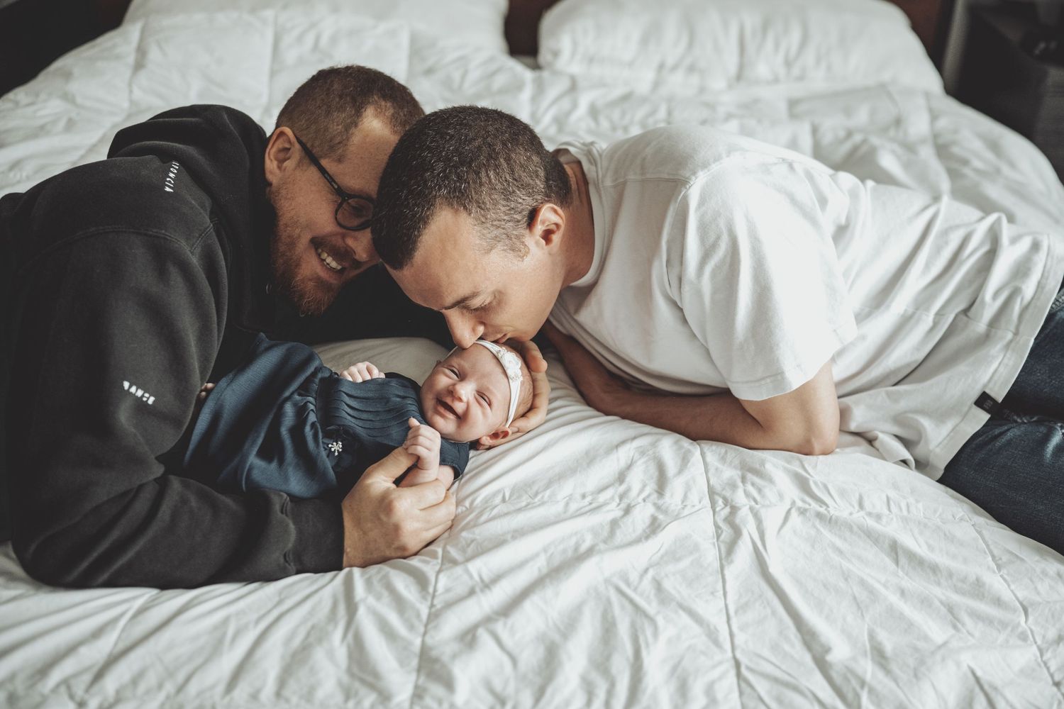 Intimate family moment captured on white bedding with natural light.