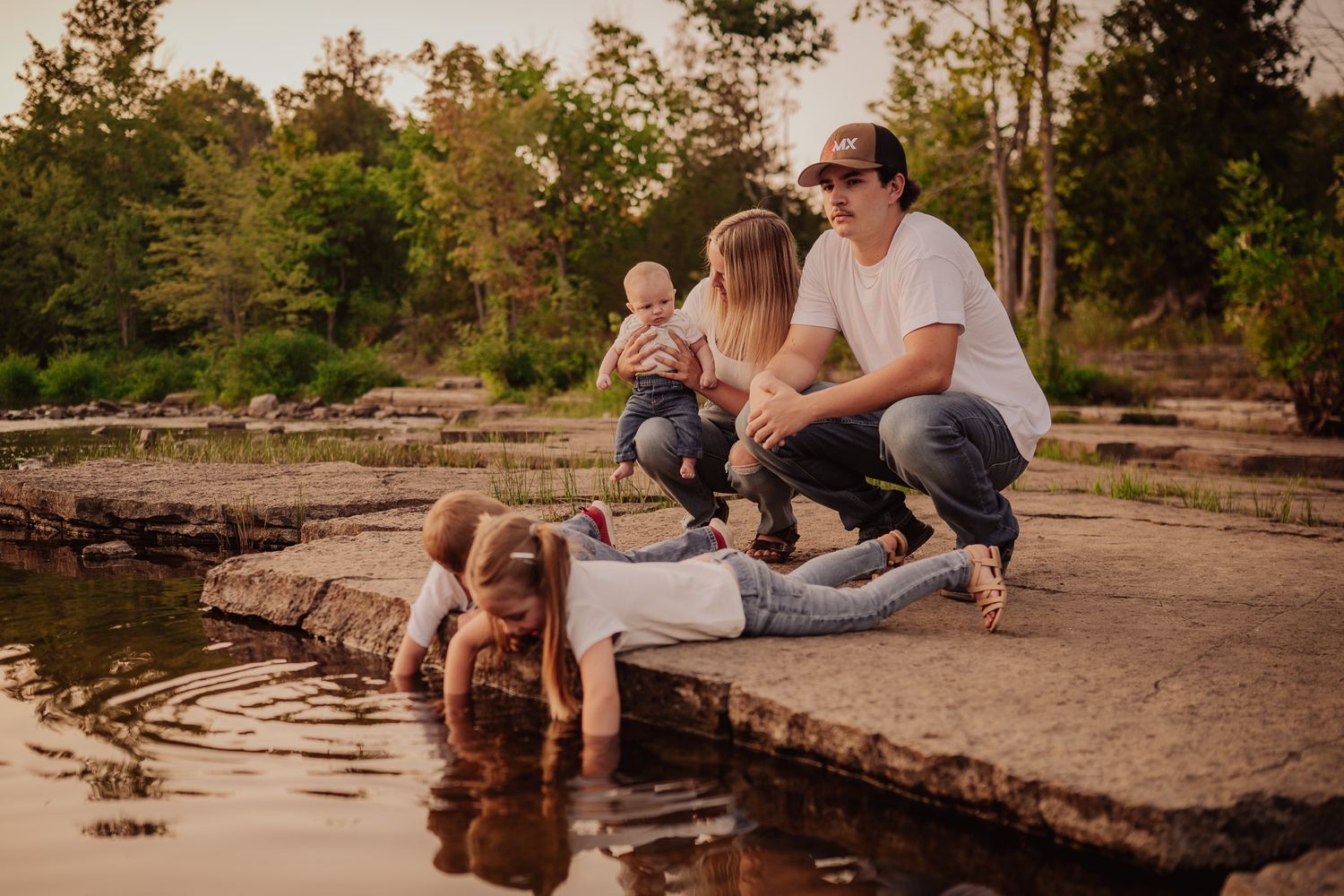 A family enjoys a peaceful moment together on a stone ledge by a tranquil pond in a natural outdoor setting.