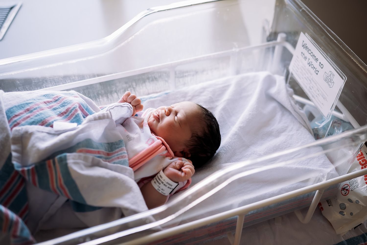 Newborn baby lying in a hospital bassinet, wrapped in a striped blanket in a maternity ward.