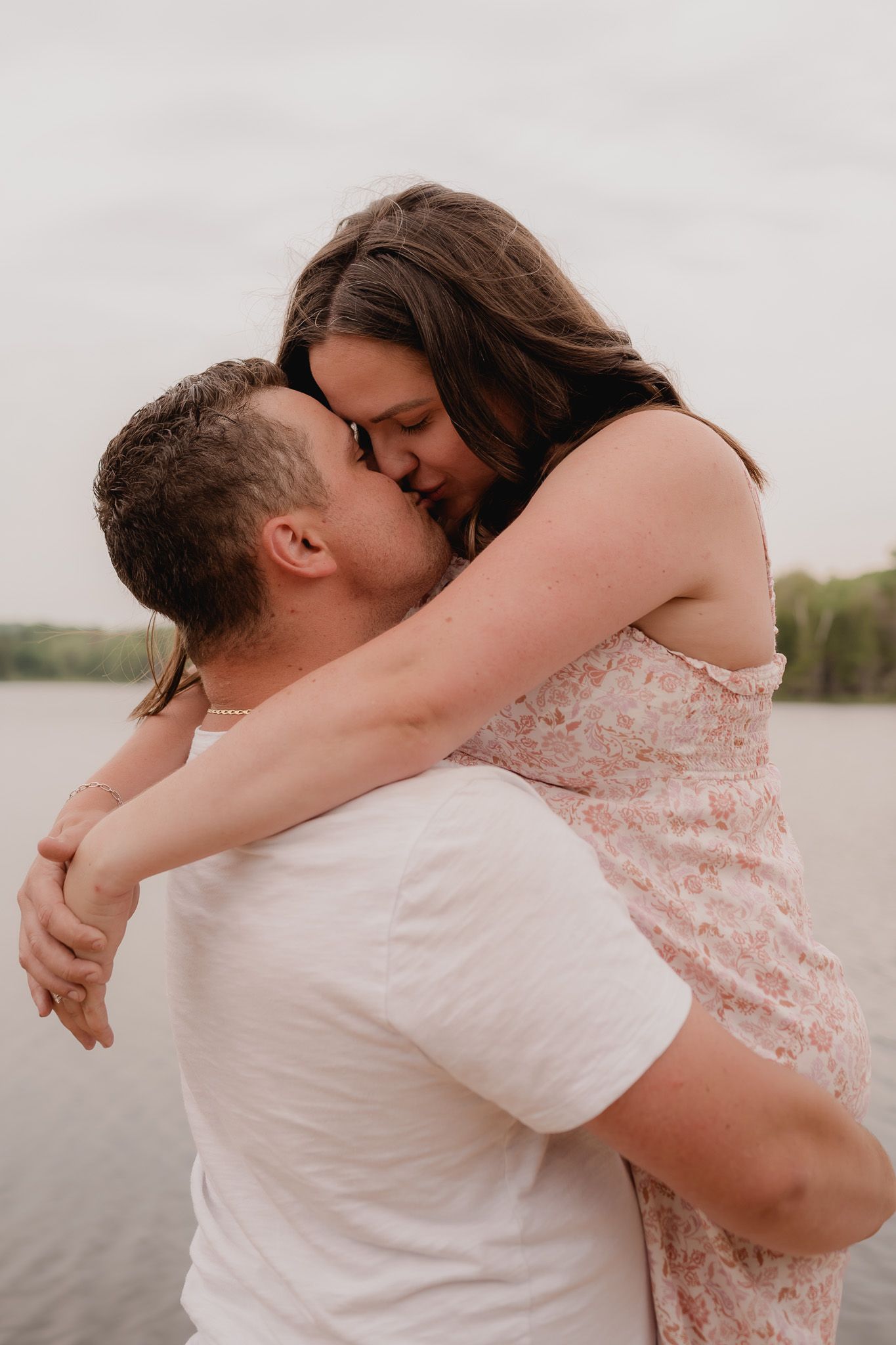A romantic couple embraces by a lake in a series of intimate photos showing them hugging and sharing tender moments.