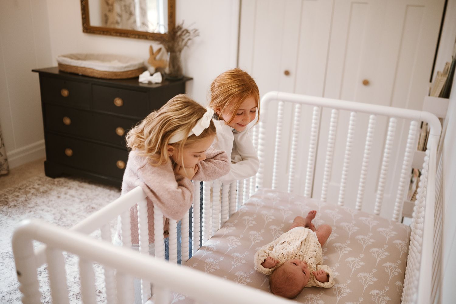 A tender moment shared between a parent and baby in a white nursery with natural light streaming through the window.