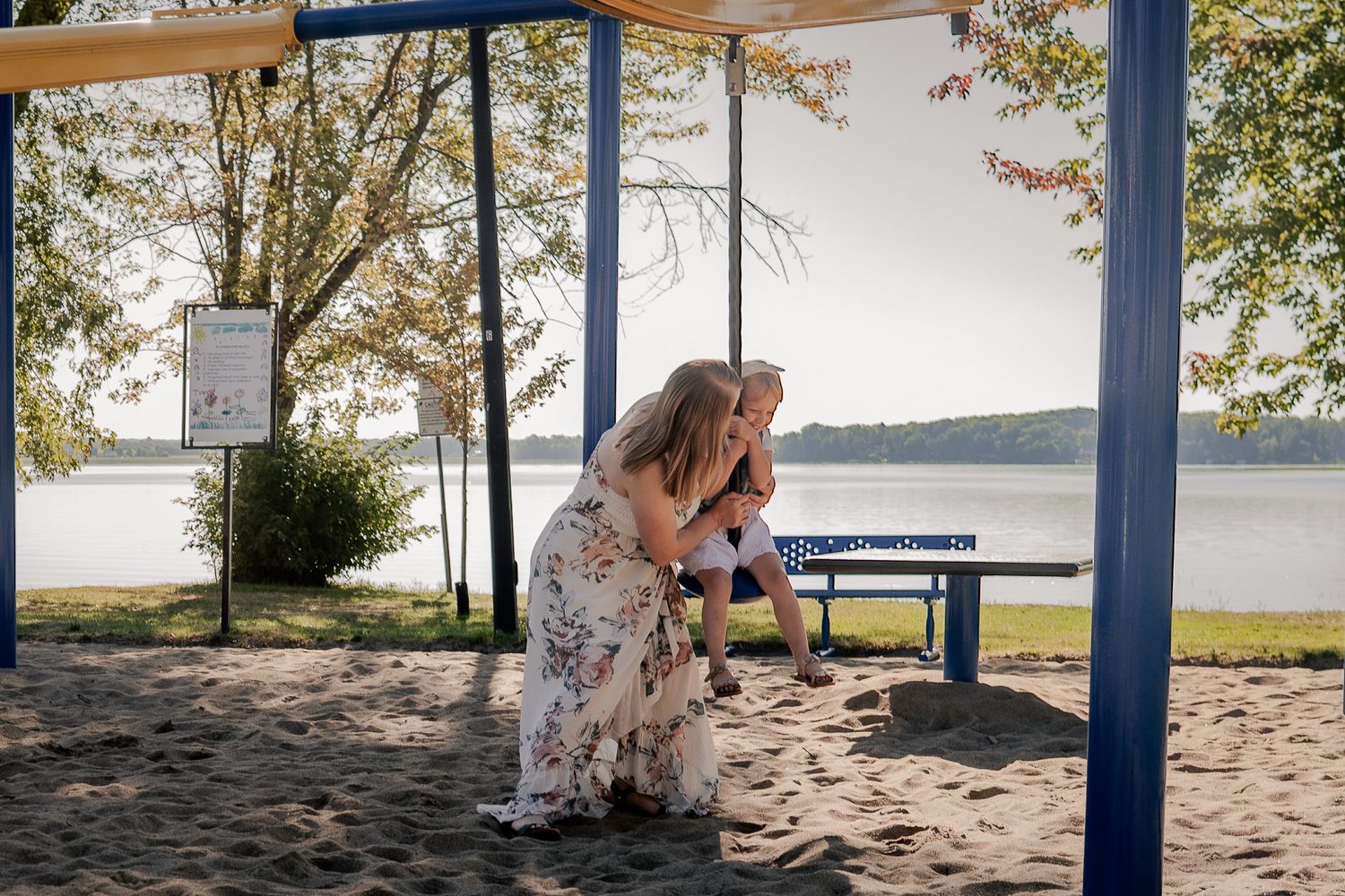 Person in a floral dress sitting on a bench by a peaceful lakeside.