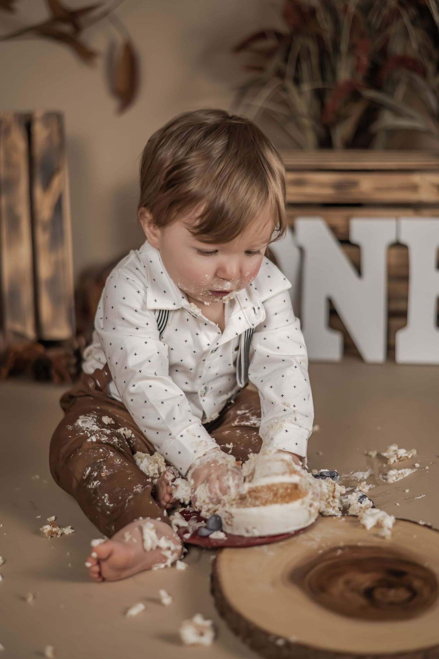 A child in a polka dot shirt plays messily with cake during a cake smash photo session.