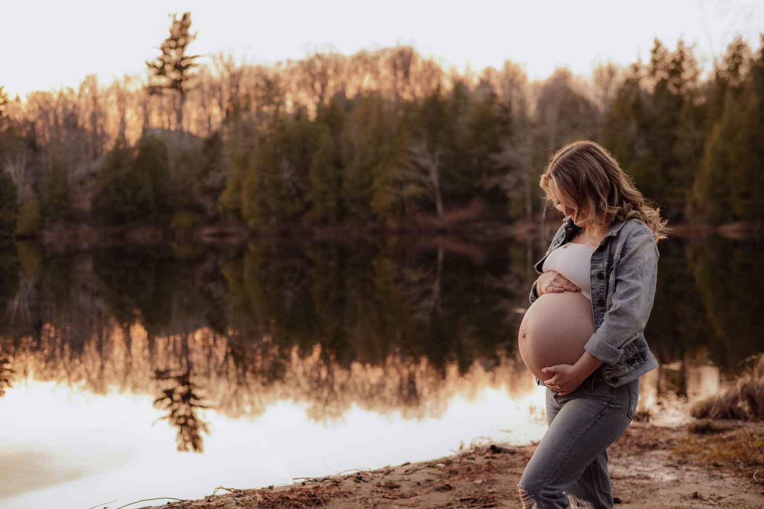 Winter maternity session by a frozen lake with evergreen trees in background. Maternity photographer Ontario