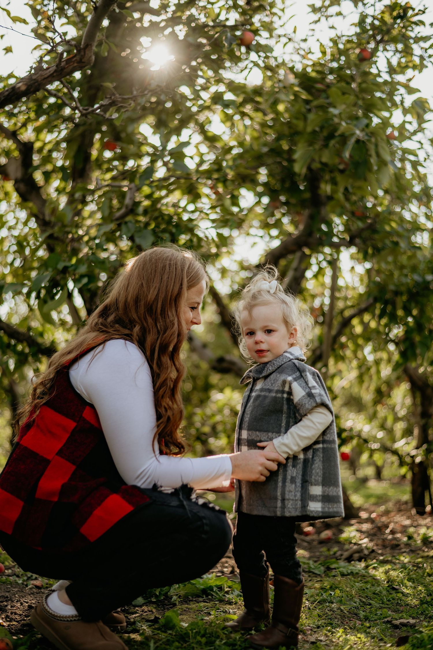 Two people share a tender moment in an apple orchard on a sunny autumn day with sunlight filtering through trees.