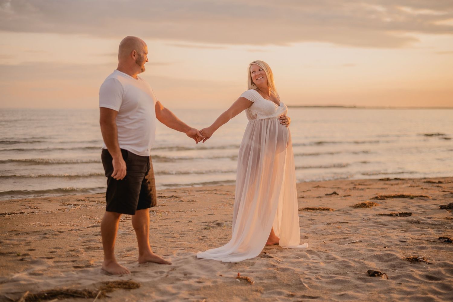 Sunset beach photoshoot with couple walking hand in hand along sandy shoreline. Maternity photographer Ontario