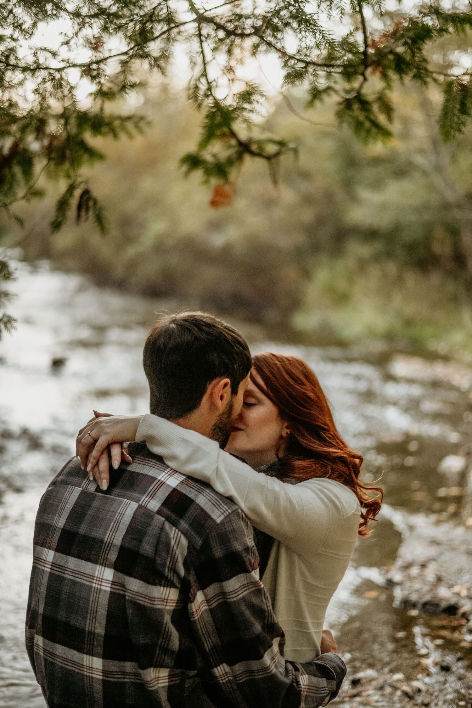 A romantic couple shares tender moments by a stream while wearing cozy fall attire.