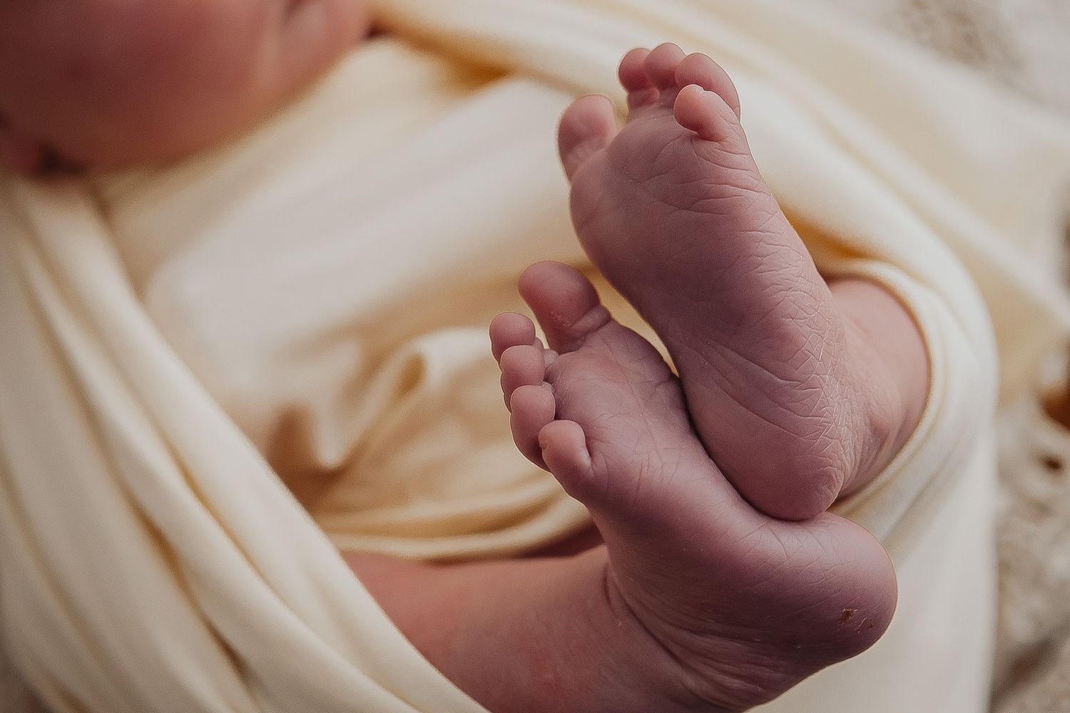 Close-up detail shot of tiny newborn feet wrapped in cream-colored fabric.