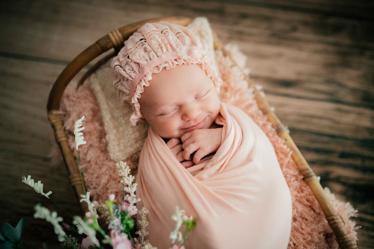 Newborn wrapped in pink fabric rests peacefully on textured basket backdrop.