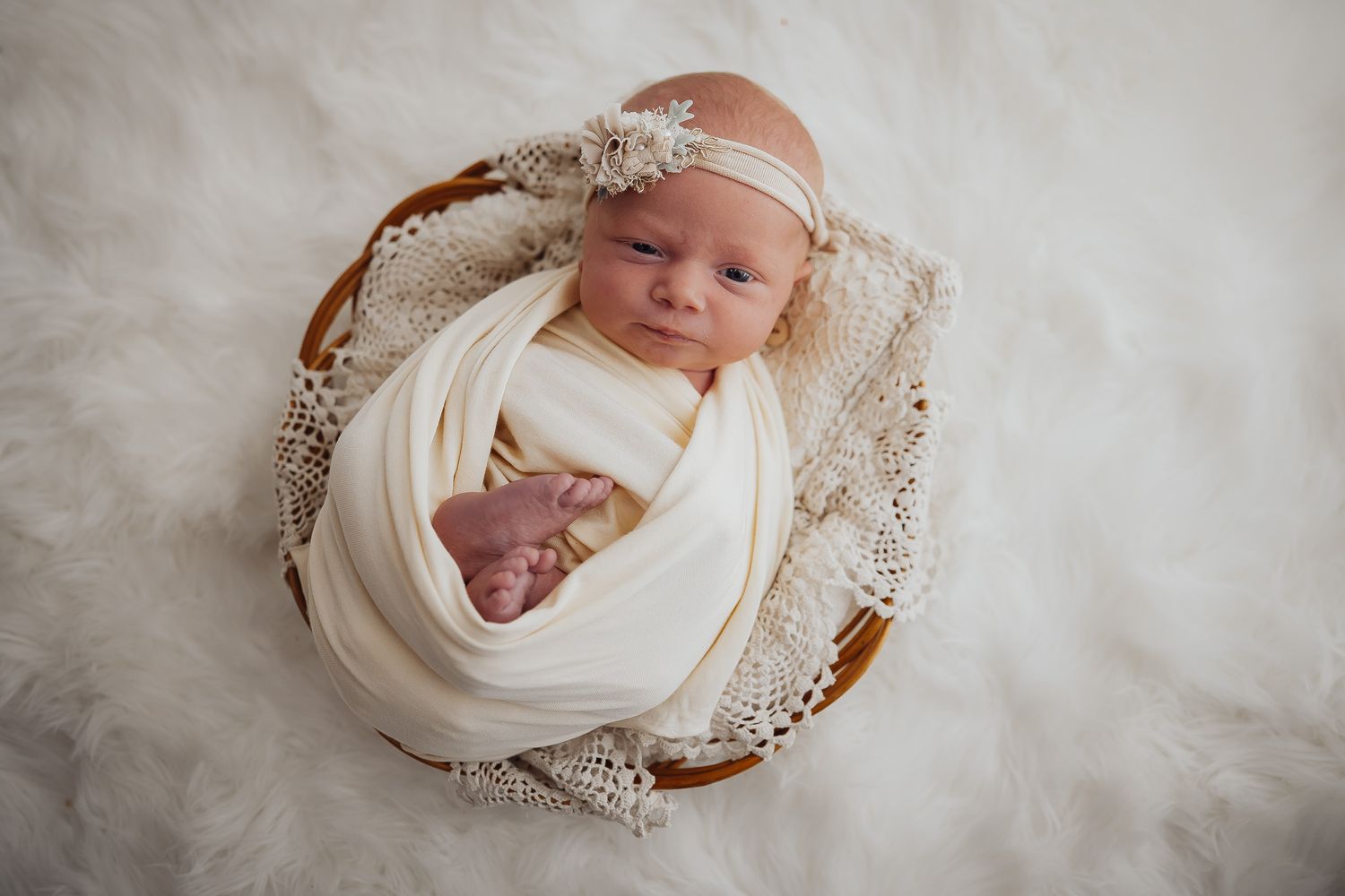 Overhead view of newborn wrapped in cream fabric lying in decorative wooden bowl.