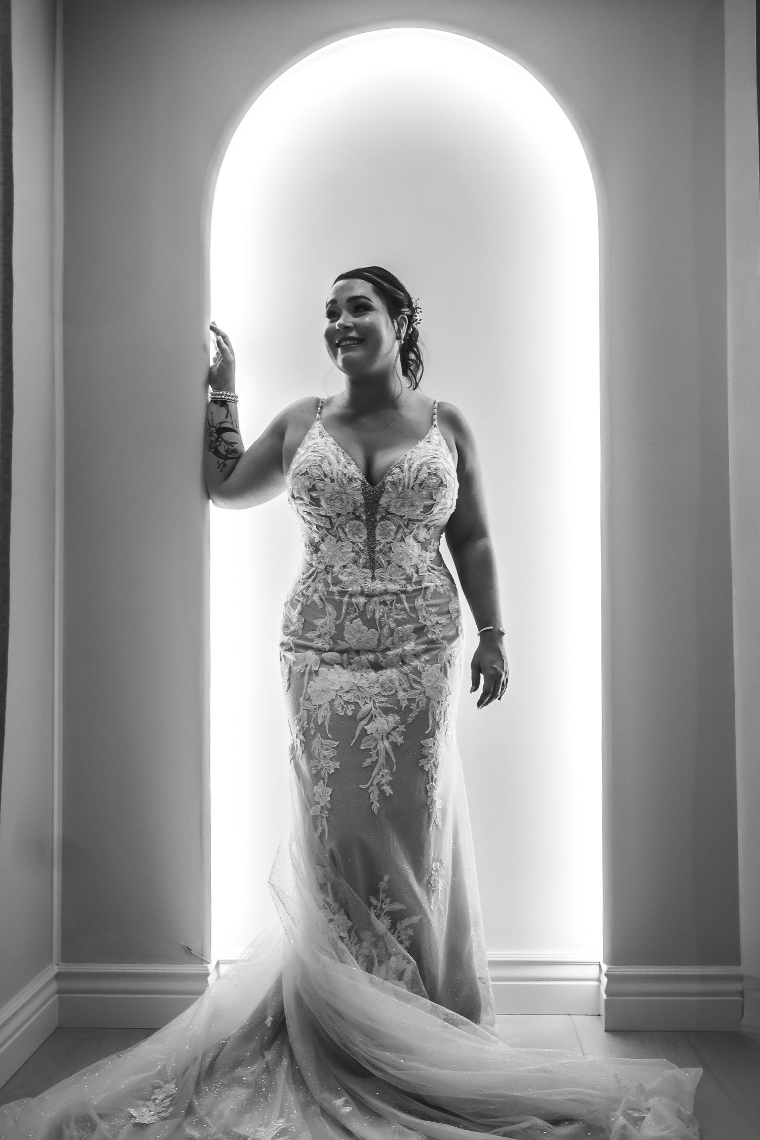 A dramatic black and white bridal portrait series showing a wedding dress with intricate lace details against illuminated arches.
