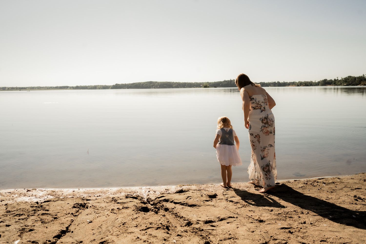People walking along a serene beach shoreline at sunset with calm waters and sandy terrain stretching into the distance.
