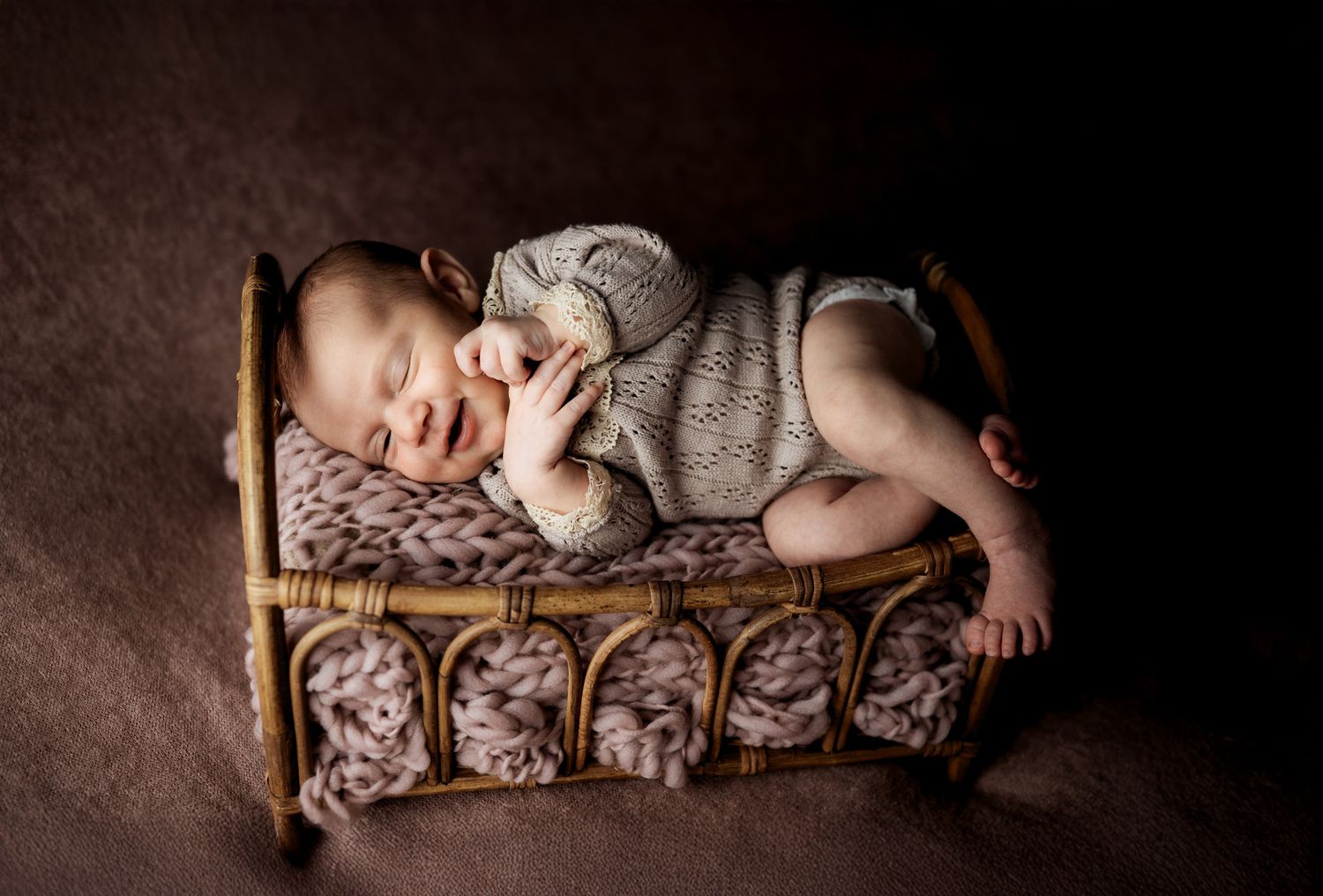 A sleeping baby in a gray sweater lies peacefully on an antique-style wooden bed with patterned bedding.