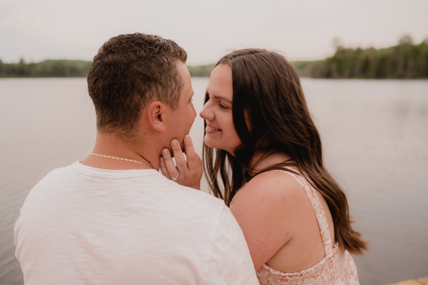 A couple in white clothing shares an intimate moment by a lake during sunset.