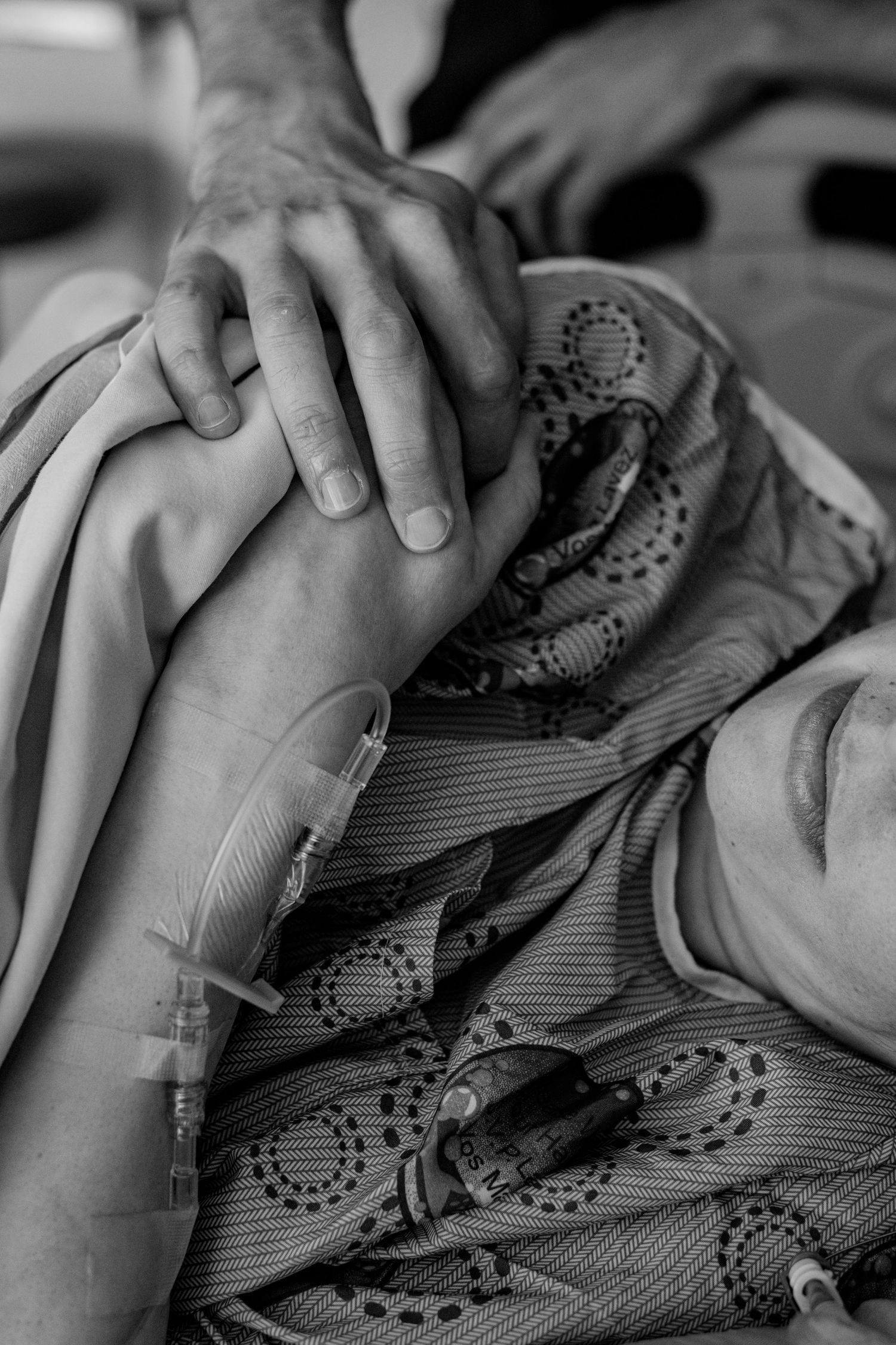 Hands gently resting on patterned hospital gown with medical tubes visible. Birth Photographer Ontario