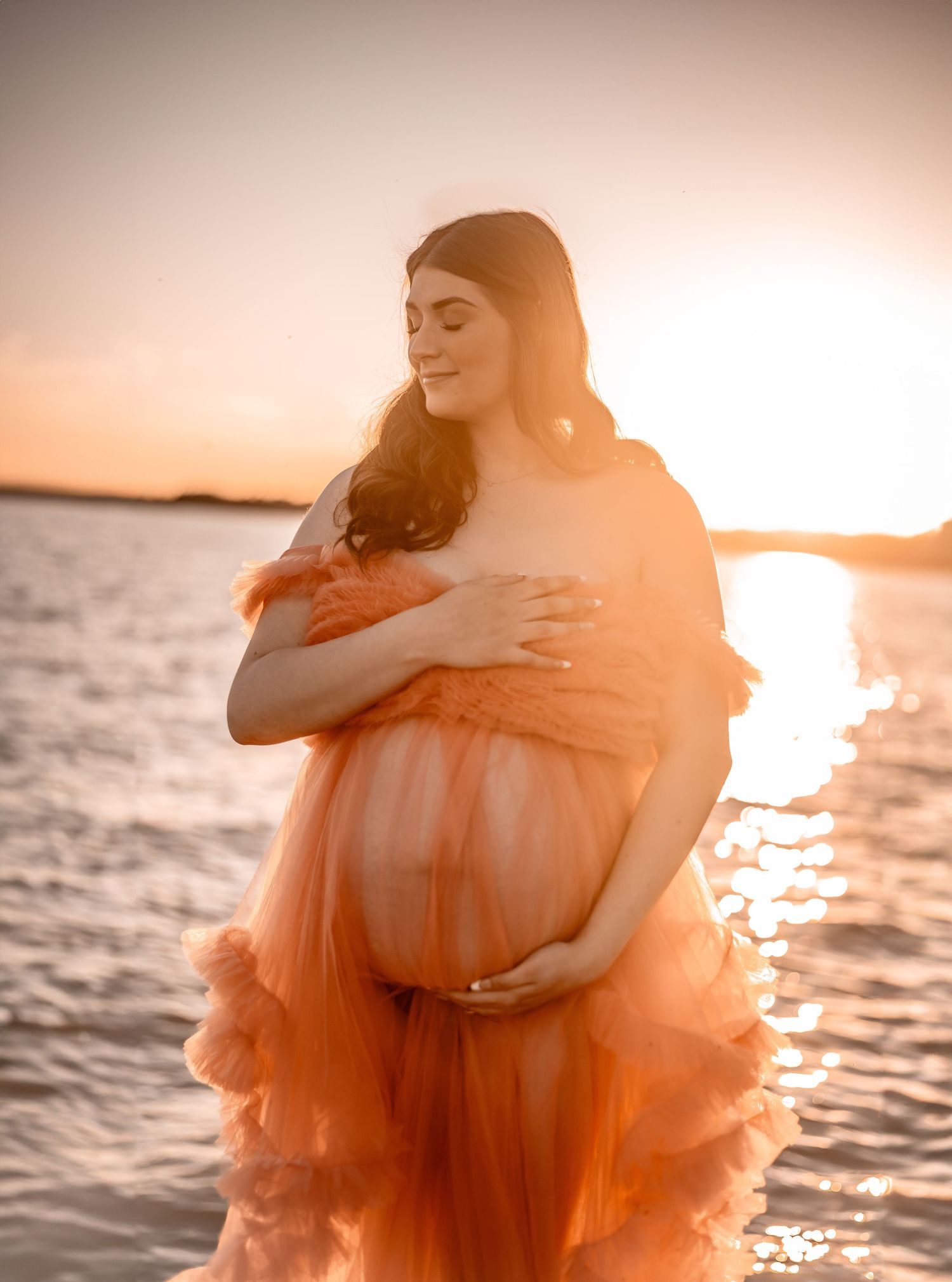 A peachy sunset illuminates a flowing dress during a waterfront maternity session. Maternity photographer Ontario